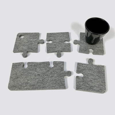 Recycled polyester felt jigsaw puzzle coasters with 4 pieces separated with a black slim cup placed on one on the upper right corner.