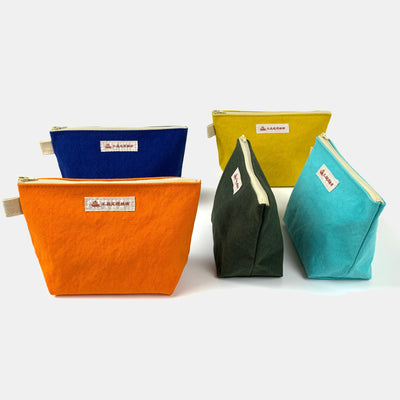 Standing view of canvas makeup bag: front left (orange), front middle (forest green), front right (sky blue), back left (klein blue), back right (mustart).