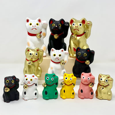 Maneki neko figurines in all 3 sizes and 6 colors. Top row from left: large white, black, gold. 2nd row from left: medium gold, white, black. Bottom row from left: small black, white, green, yellow, pink, gold.