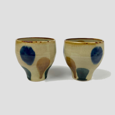 Close-up of ceramic tea cups with a pattern of blue, ochre and green drops.