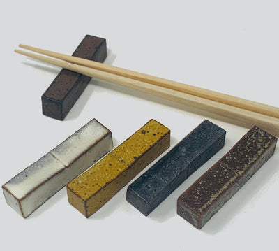 A set of 5 ceramic chopstick rests in 5 colors. A set of chopsticks is placed on one of the chopstick rests.