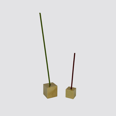 A large gold cube incense holder with a green incense stick on the left and a small gold cube incense holder with a brown incense stick on the right.