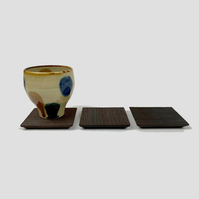 3 kiri coasters. The one on the far left holds a ceramic tea cup with blue, ochre and green drops.